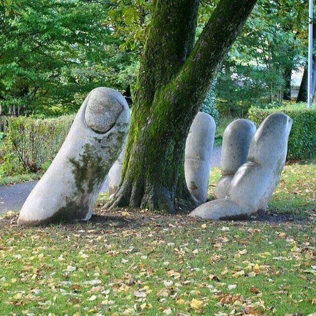 Große Hand-Skulptur, die aus dem Boden neben einem Baum greift